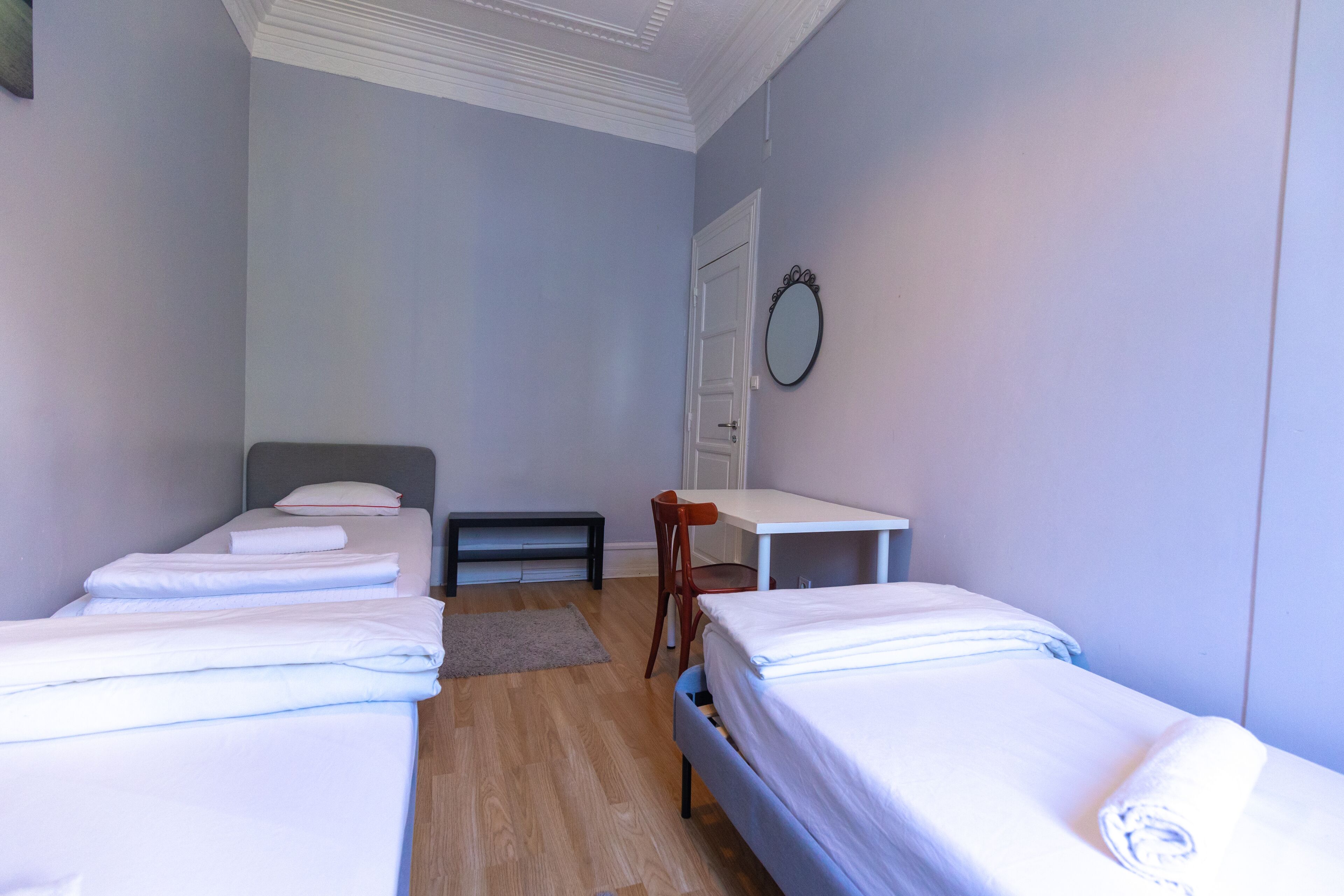 A small, clean room with two single beds, a desk, a chair, and a mirror on the wall.