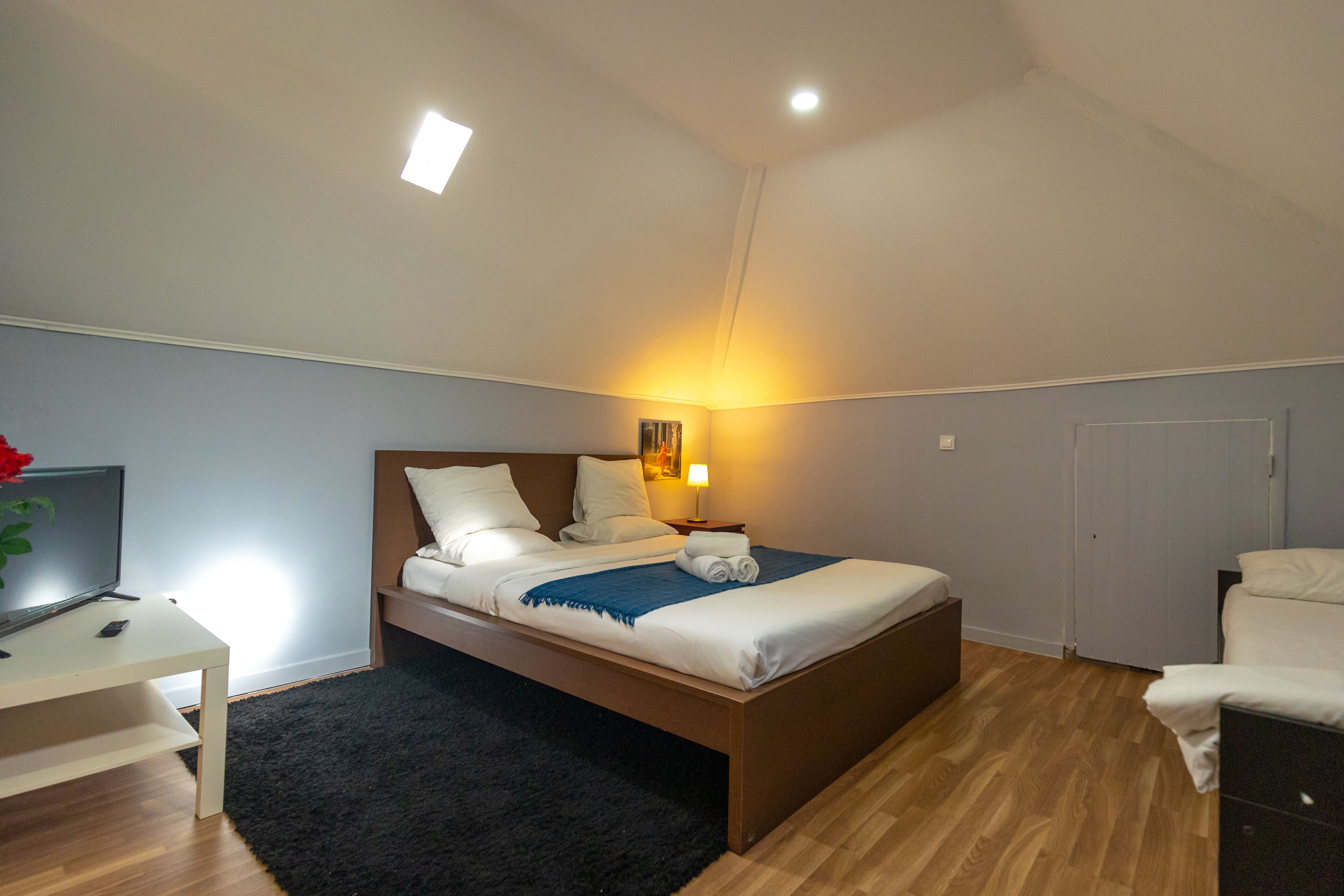 A bedroom with a bed, bedside table, lamp, and a TV.