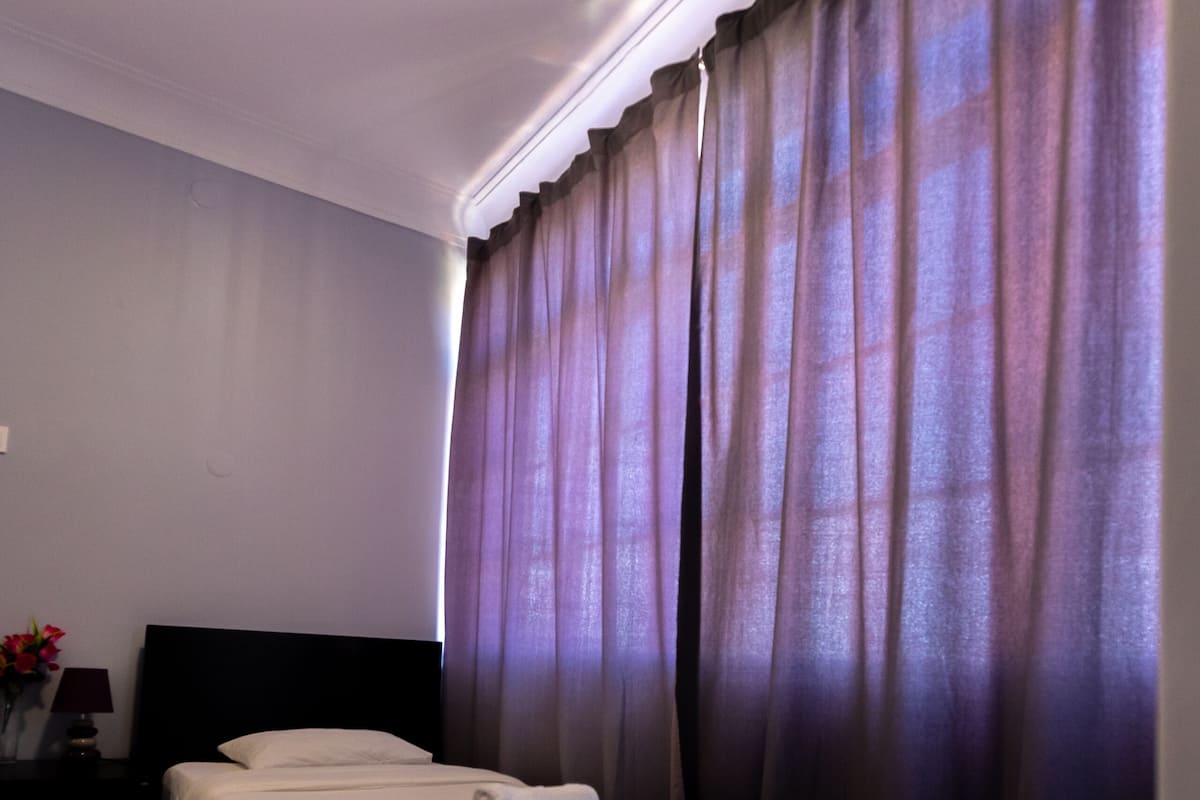 Un dormitorio con cama, cortinas oscuras, una mesita de noche y una lámpara.