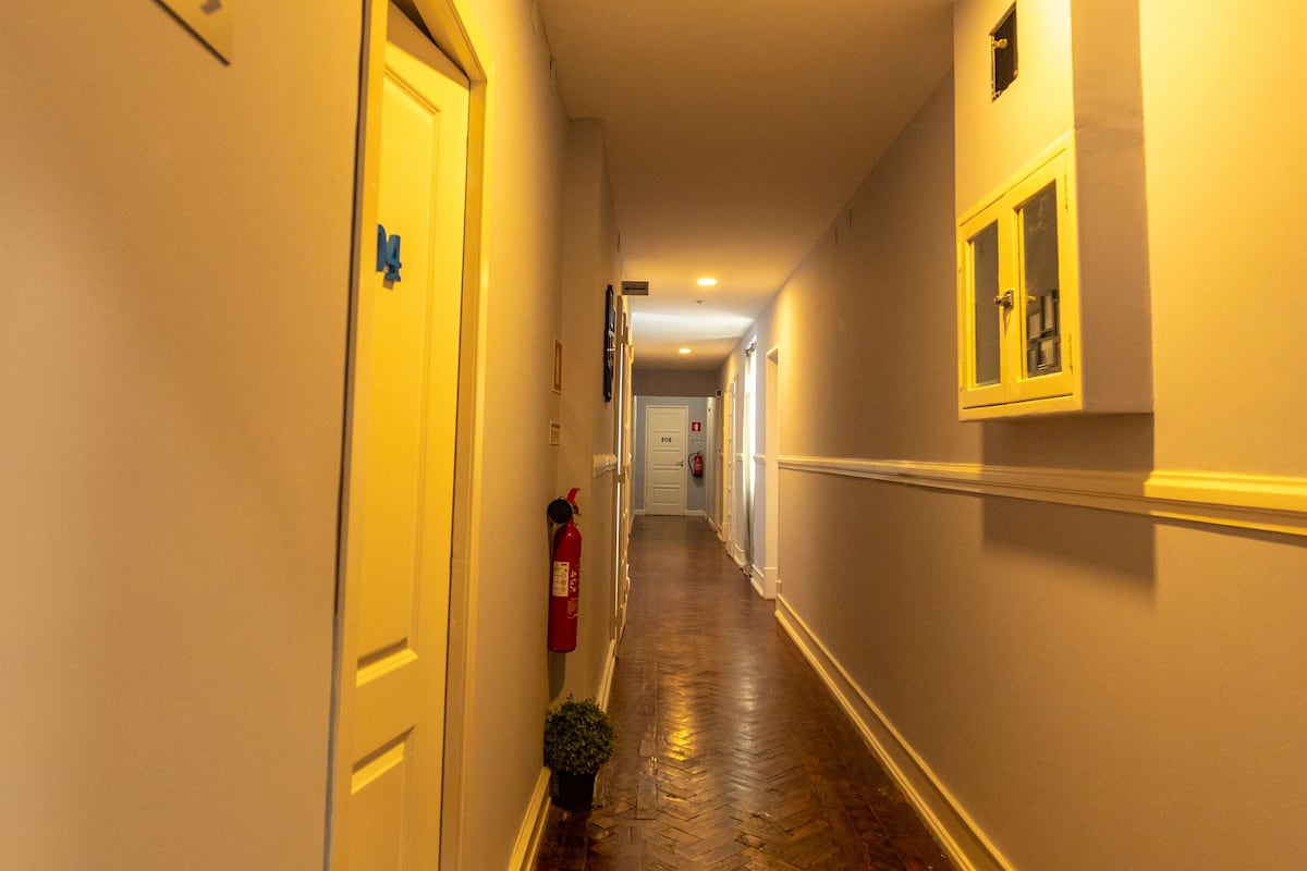 Un pasillo con suelo de madera, un extintor y una puerta con un cartel de número.