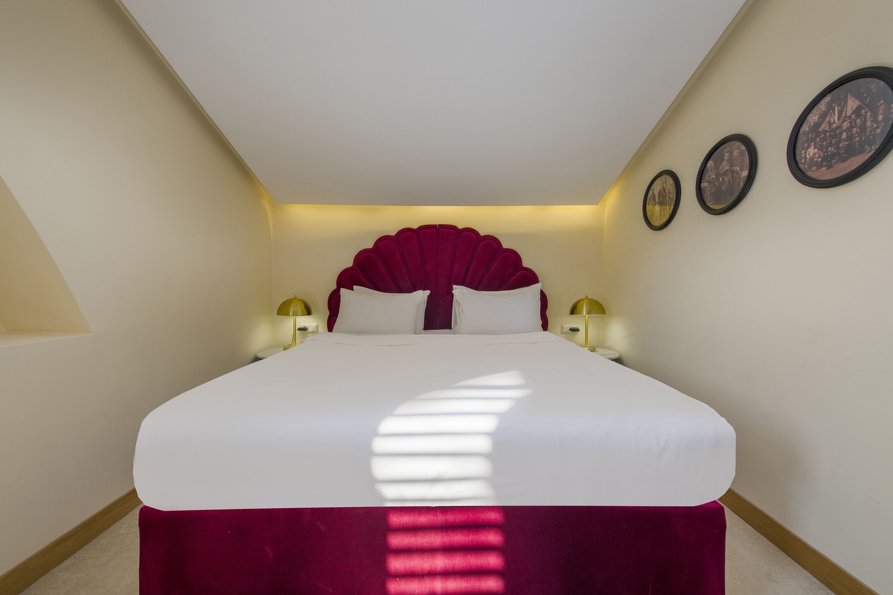 A large bed with a white headboard and a red skirt, two bedside lamps, and three framed pictures on the wall.