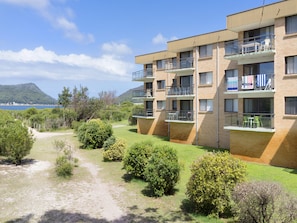 Een meerlaags appartementencomplex met balkons, een helder uitzicht op de zee en een glooiend landschap op de achtergrond.