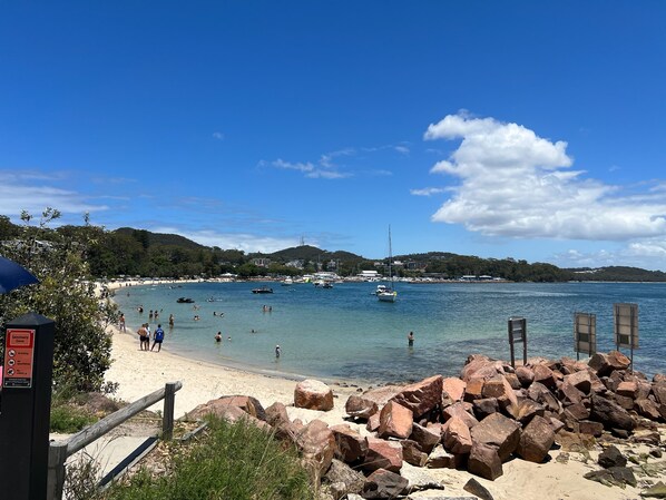 A beach with clear water, boats, and a rocky shoreline.