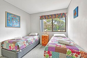 A bedroom with two single beds, a wooden dresser, and a window with a view of trees. - Foreshore Paradise Nelson Bay (Nelson Bay)