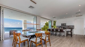 Una cocina moderna con una isla grande, un comedor con mesa de vidrio y vista al océano.
