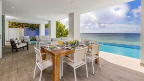 Un comedor con vista al océano, una piscina y un diseño interior moderno.