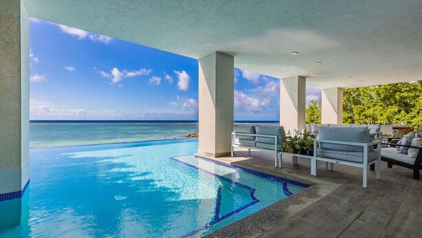 Una piscina infinita con vistas claras al océano, asientos exteriores y un entorno tropical.
