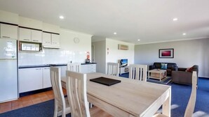 A modern kitchen with white cabinets and a dining area with a wooden table and chairs. - Horizons Retreat (Salamander Bay)