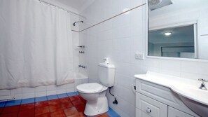 A bathroom with a white toilet, a shower, and a sink with a mirror.