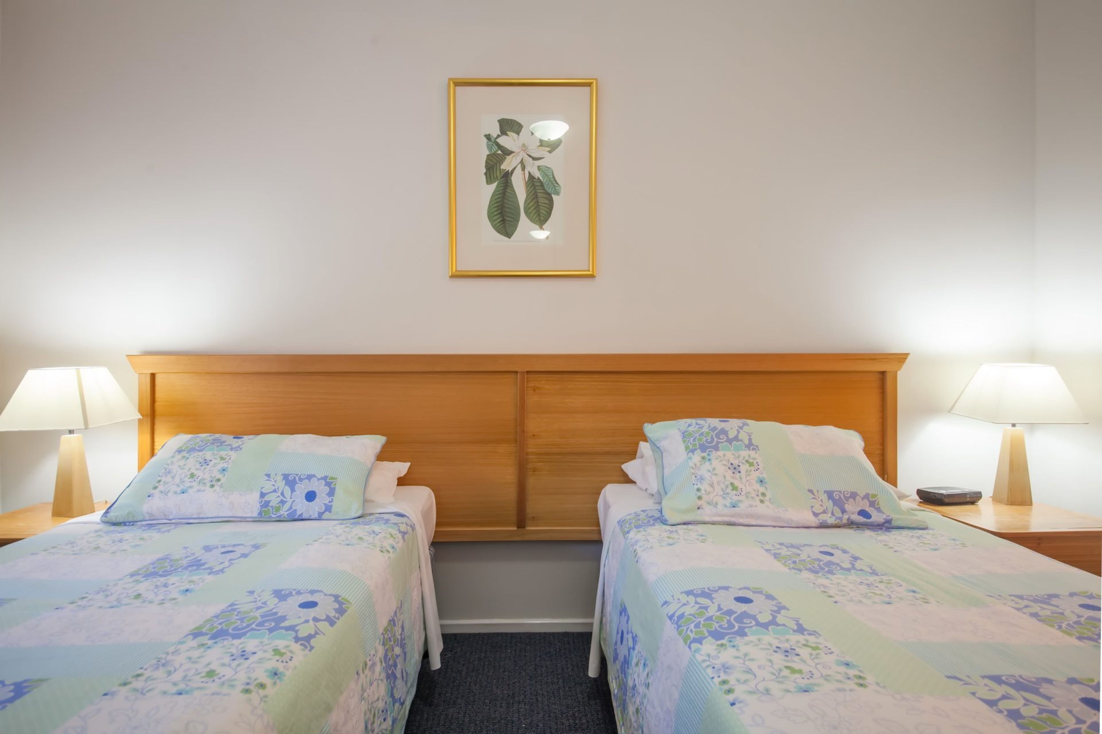 A hotel room with two single beds, a wooden headboard, and a framed botanical print on the wall.