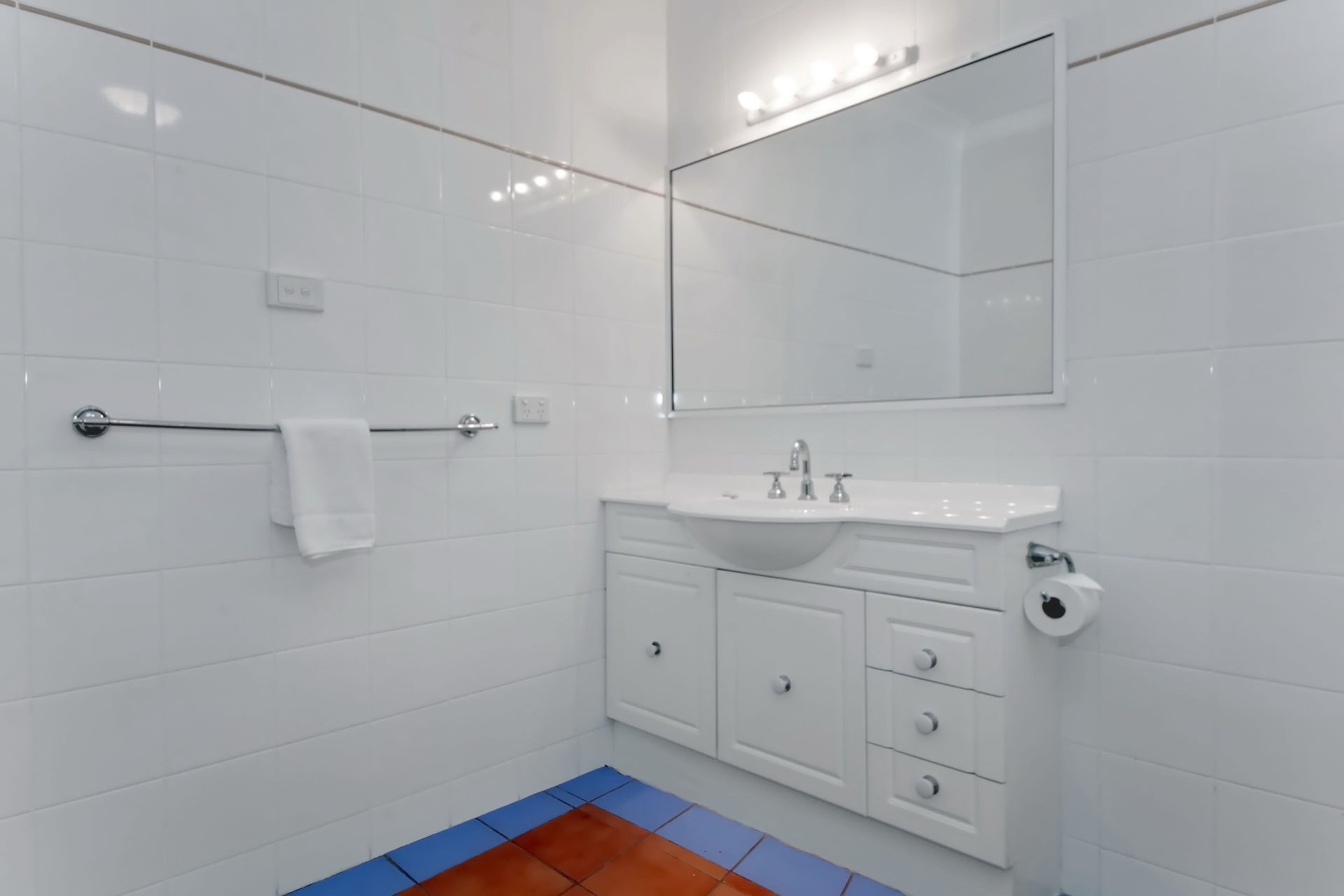 A modern bathroom with white tiles, a sink, a mirror, and a towel rack.