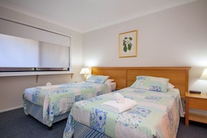 A hotel room with two beds, a large window, a wall-mounted TV, and a framed botanical print.