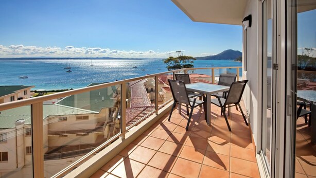 Un balcone con vista sul mare, un tavolo con sedie e una porta vetrata.