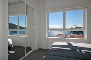Een slaapkamer met een groot raam met uitzicht op een wateroppervlak en een heuvellandschap.