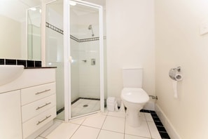 Een badkamer met een douchecabine van glas, een wit toilet en een wastafel met een zwarte tegel aanrecht.