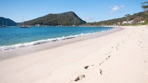 Une plage avec une eau d’un bleu limpide, un rivage sablonneux et une montagne en arrière-plan.