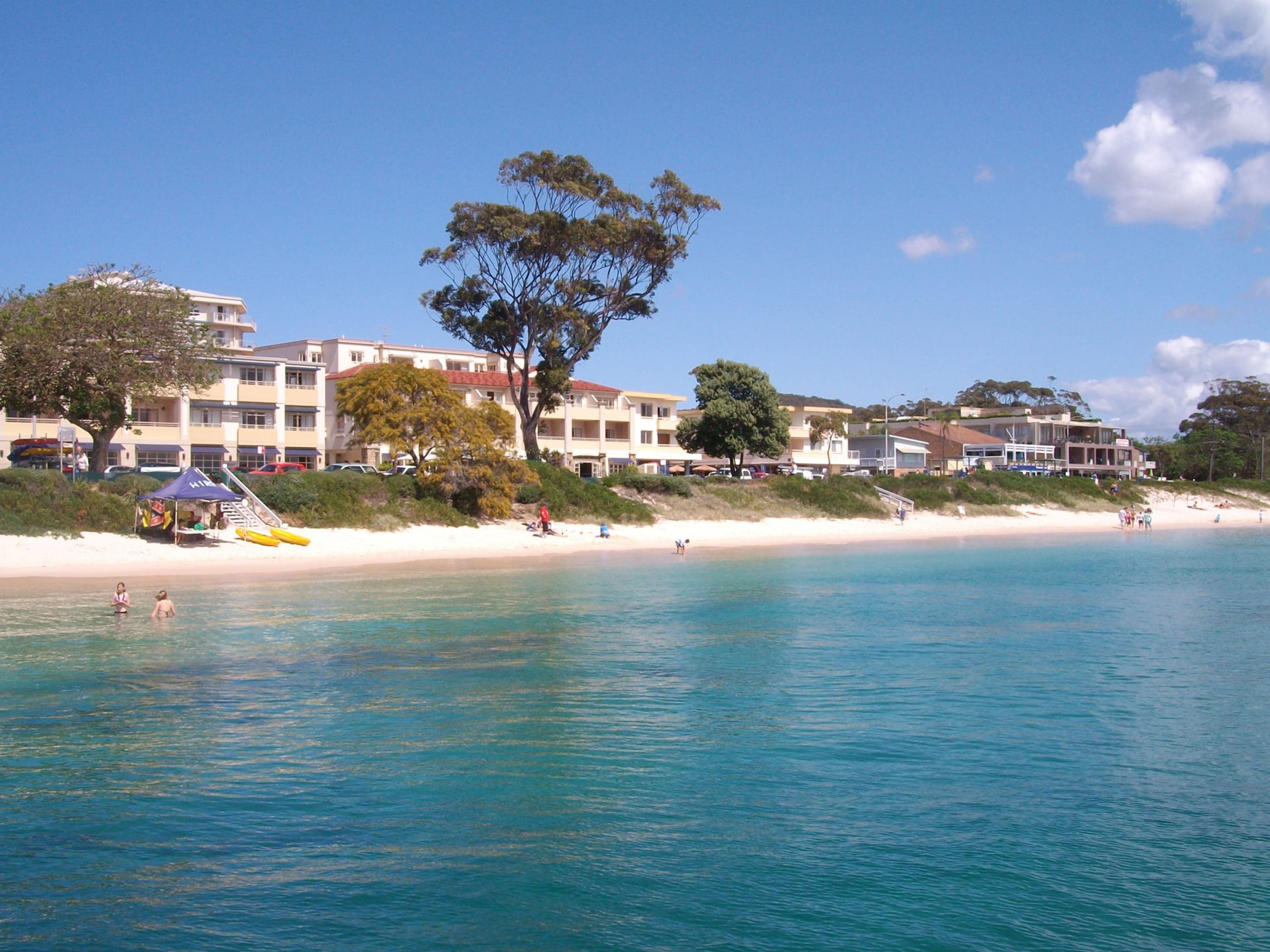 A beachfront hotel with multiple-story buildings, a sandy beach, and clear blue waters.