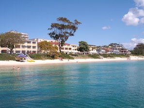 A beachfront hotel with multiple-story buildings, a sandy beach, and clear blue waters.