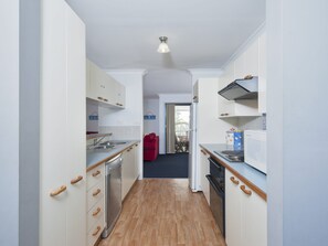 A narrow kitchen with wooden flooring, white cabinets, and a red chair in the background. - Carindale 21 Nelson Bay Apartment with Pool (Nelson Bay)