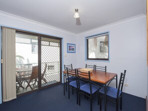 A dining area with a table and chairs, a window, and a door with a mesh screen. - Carindale 21 Nelson Bay Apartment with Pool (Nelson Bay)