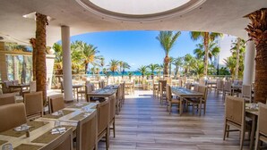 Ein Restaurant mit Meerblick, mit Holztischen und -stühlen sowie Palmen.