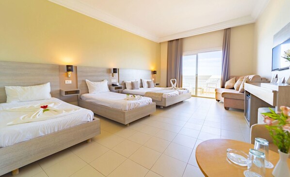 A hotel room with three beds, a sofa, a desk, and a balcony with a view.