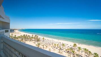 A beach view from a balcony with palm trees and umbrellas.