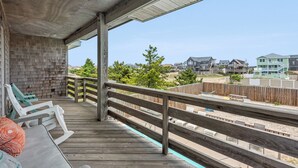 A wooden deck with a railing, a concrete ceiling, and a view of a residential area with houses and trees.