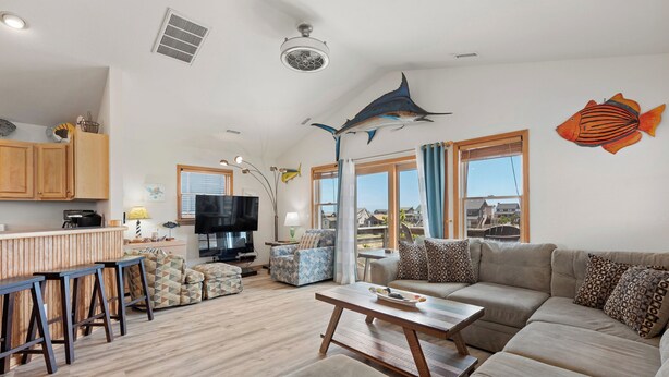 A spacious living area with a sofa, a coffee table, and a TV. There are wooden cabinets and a bar area.