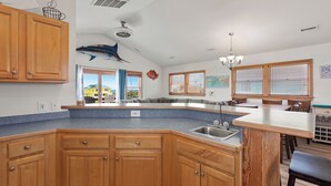 A kitchen with wooden cabinets, a large island, a fish decoration, and a view of the outside.