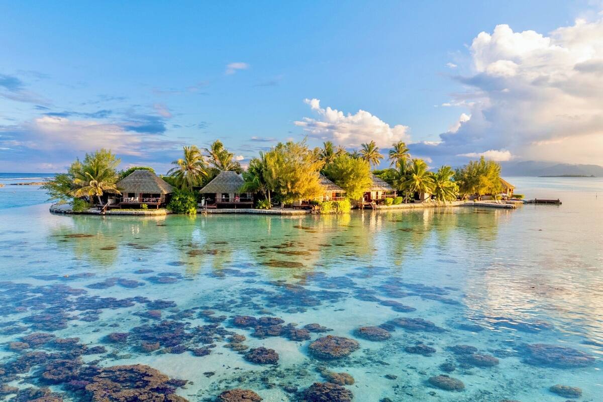 A tropical island resort with overwater bungalows, clear turquoise water, and coral reefs.