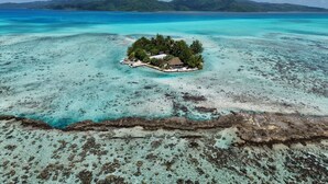 An island with a small building surrounded by trees, clear turquoise water, and distant mountains. - EDEN - Private Island - TAHA'A (Taha'a)