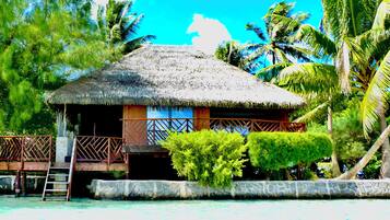 A thatched-roof hut with a wooden deck and a ladder leading to a stone platform.