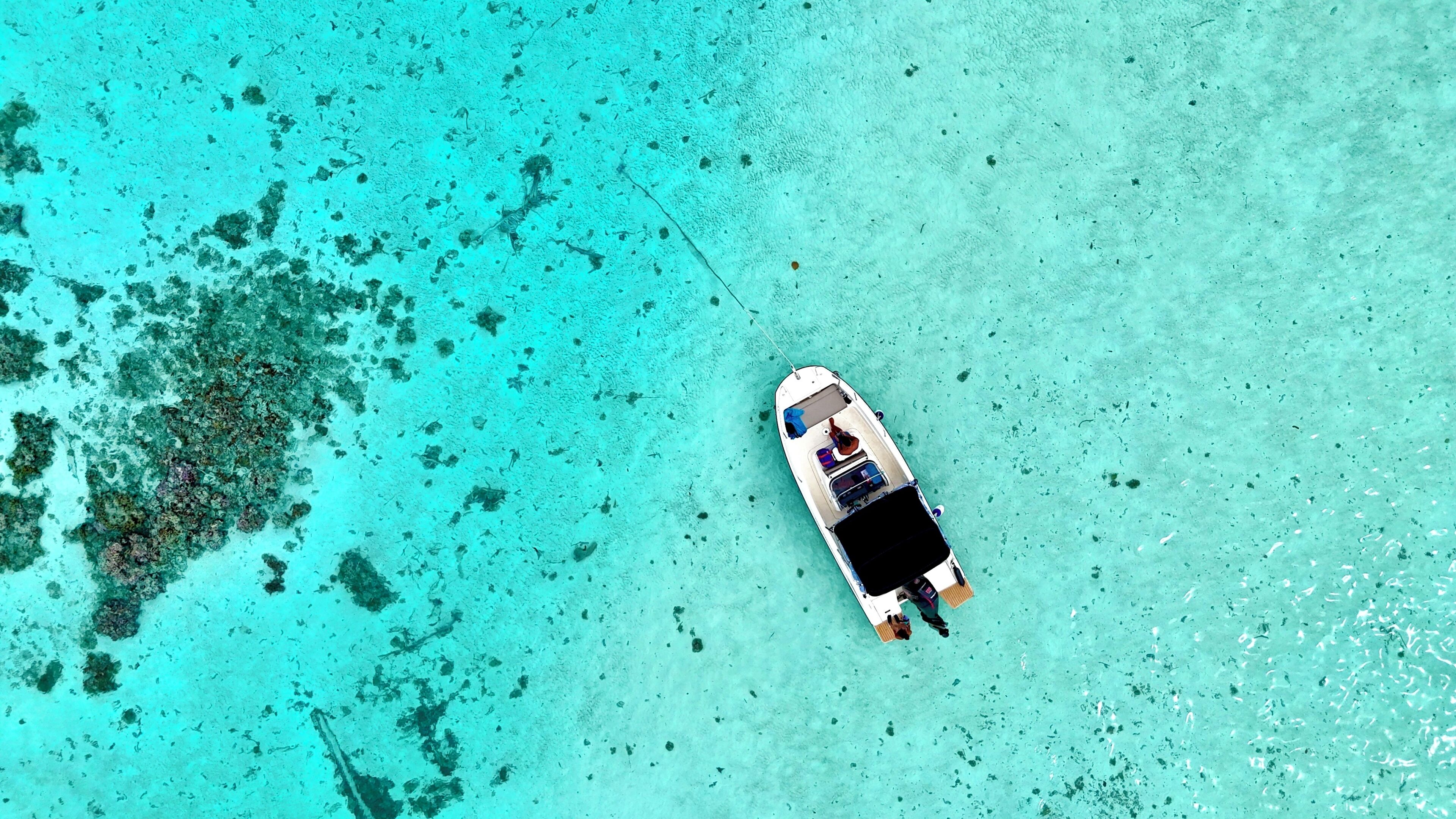 An aerial view of a boat anchored in clear turquoise waters with visible coral formations nearby.