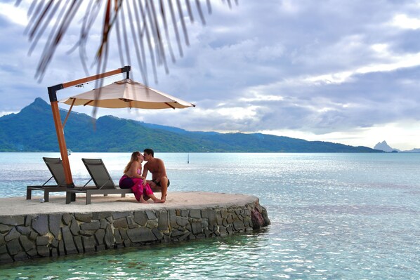 A couple sitting on a stone platform with a beach and mountains in the background. - EDEN - Private Island - TAHA'A (Taha'a)