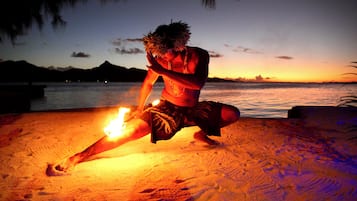 A person performing a fire dance on a beach at sunset.