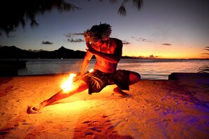 Una persona bailando con fuego en la playa al atardecer.