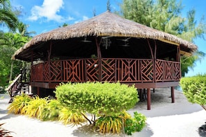 A thatched-roof structure with a wooden lattice design, situated on a sandy beach with tropical vegetation. - EDEN - Private Island - TAHA'A (Taha'a)
