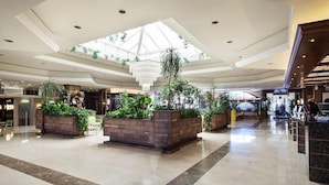 A spacious lobby with a high ceiling, large windows, and multiple planters with greenery. - Evenia Olympic Resort - Olympic Park (Lloret de Mar)