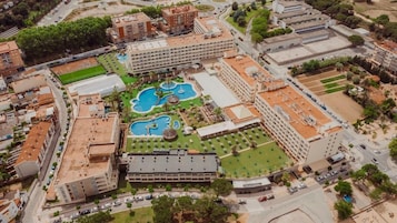 An aerial view of a hotel complex with multiple buildings, a central courtyard with pools, and surrounding greenery.