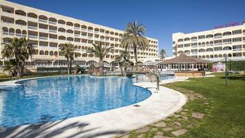 Un hôtel doté d’une grande piscine, de palmiers et d’un espace abrité.