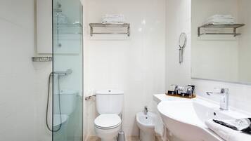 A modern bathroom with a glass-enclosed shower, a toilet, a bidet, and a sink with a mirror.