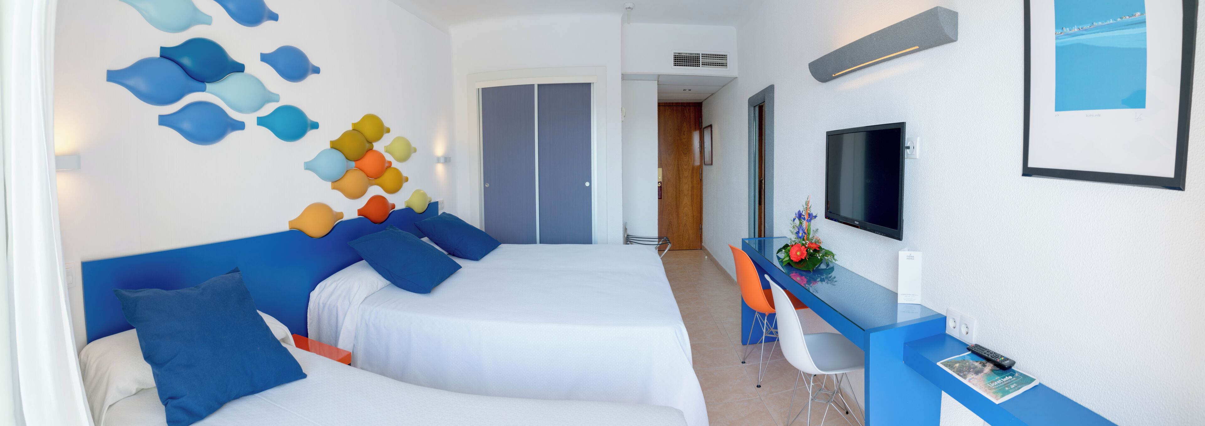 Habitació d'hotel amb un llit, una taula de treball amb una cadira, una televisió i un quadre al mur.