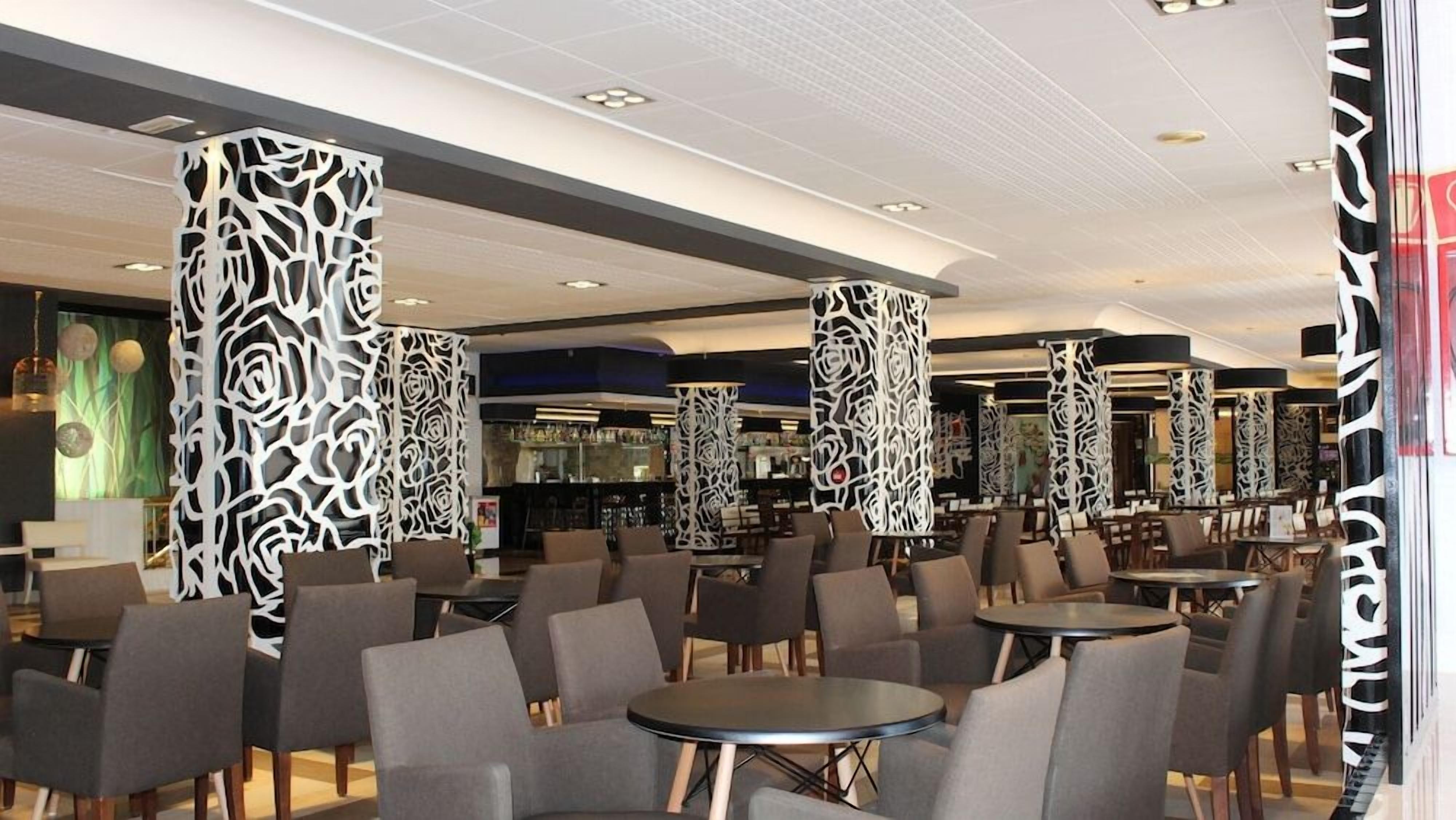 A modern interior with round tables and chairs, decorative panels, and a bar area.