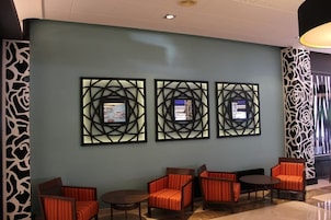 Un vestíbulo con tres obras de arte enmarcadas en la pared, una zona de estar con sillones tapizados en naranja, y un panel de pared estampado a la izquierda.