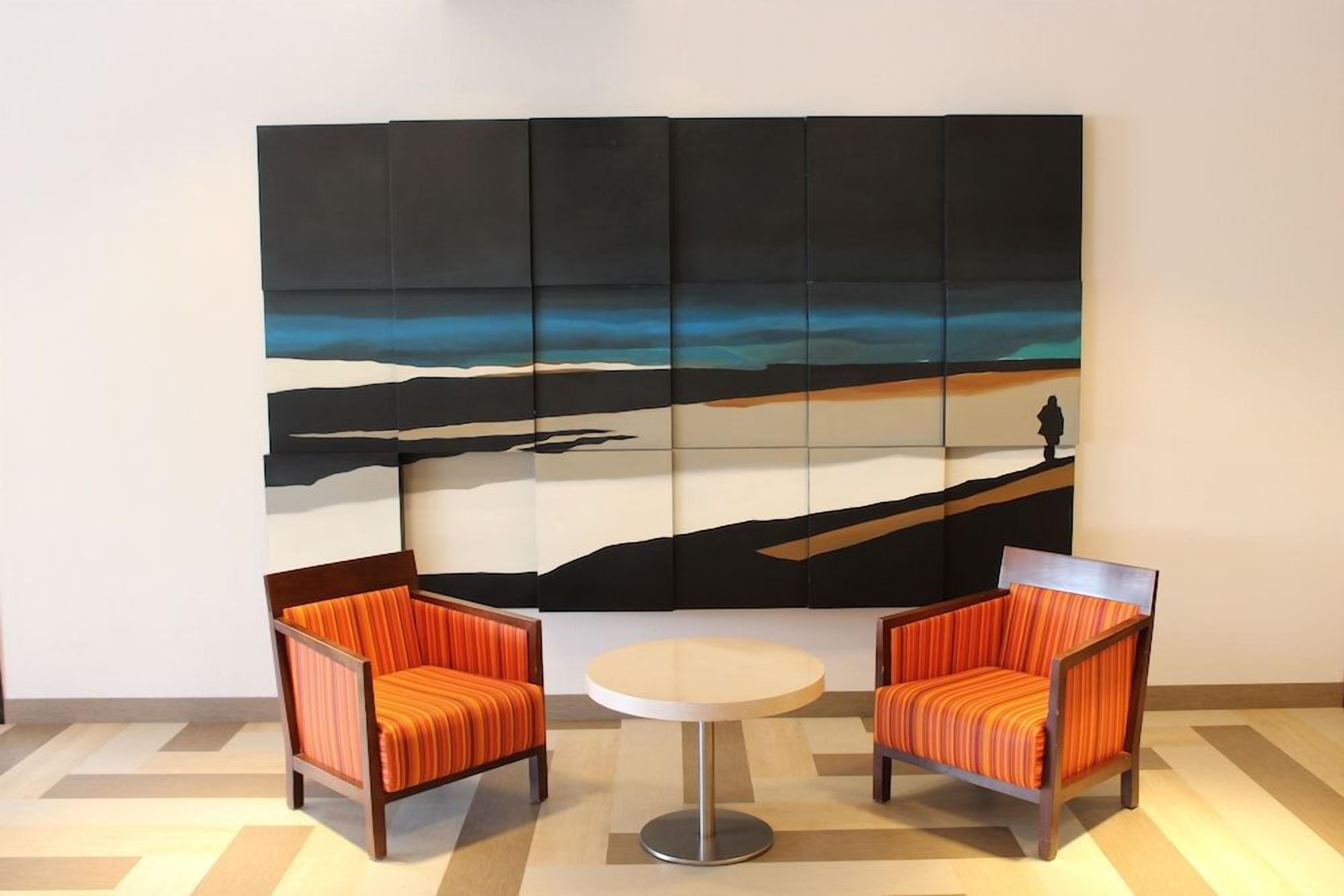 A room with two orange-striped chairs and a small round table. A large abstract painting is on the wall.