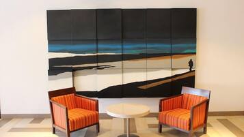A room with two orange-striped chairs and a small round table. A large abstract painting is on the wall.