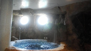 A hot tub with a rocky interior, two circular windows, and a showerhead. - Evenia Olympic Resort - Olympic Park (Lloret de Mar)