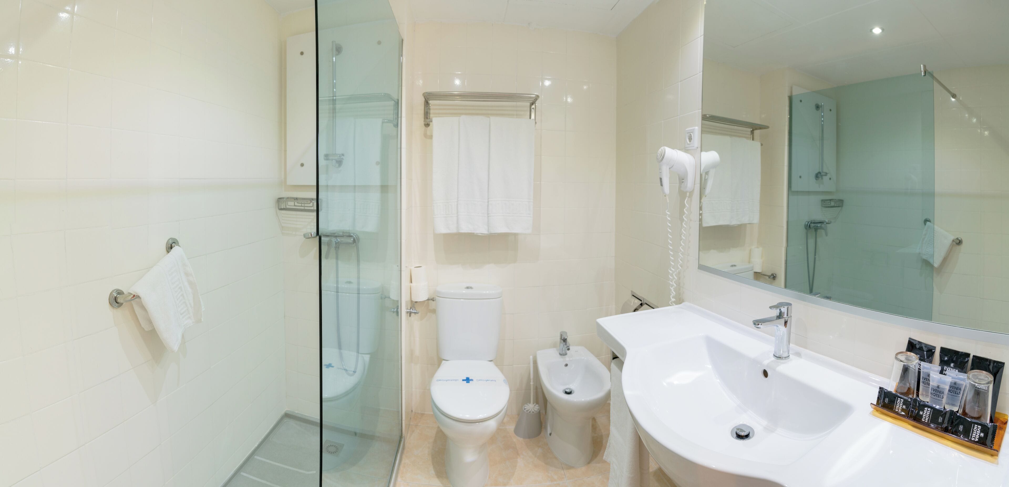 A modern bathroom with a glass shower enclosure, a toilet, a bidet, and a large sink with a mirror.