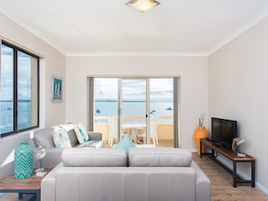 Een moderne woonkamer met een bank, een televisie en uitzicht op zee door grote schuifdeuren.
